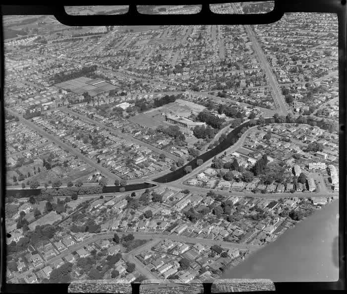 An aerial view of Avonside Girls' High School and Wilding Park in the background, including Avon River in the foreground, Christchurch, 1950