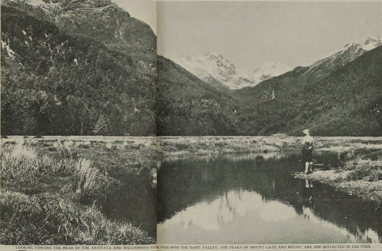 A woman standing on the bank of the Arawata River, snow-covered Mount Gate and Mount Ark in the background, 1938