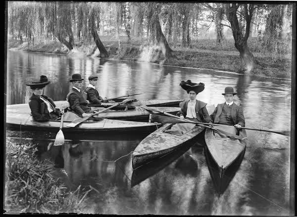 Three men and two women in tethered canoes, 1900