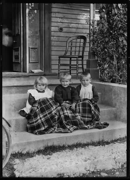 Three small children outside a house, 1900