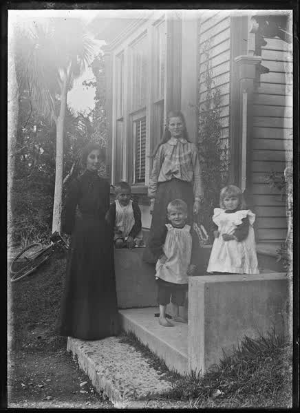 Woman, girl and three children outside a house, 1900