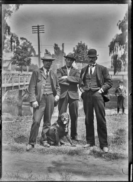 Three men standing on the bank of the Avon River with a dog, 1900