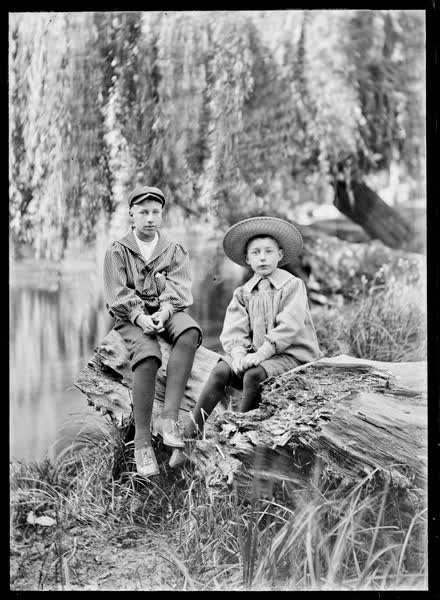 Two boys seated on a log, 1900