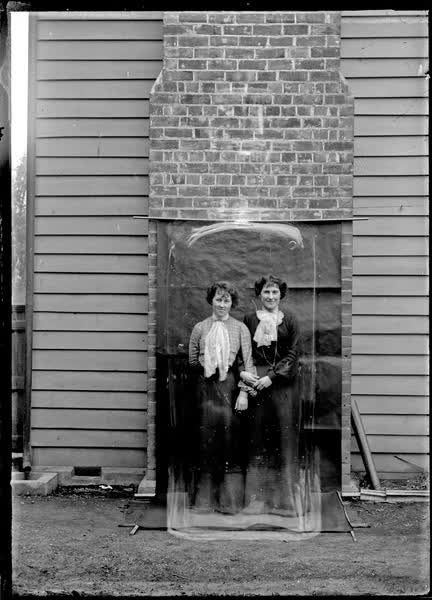 Two women standing on a drop-cloth background, 1900