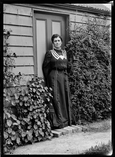Woman standing on the doorstep of a weatherboard house, 1900