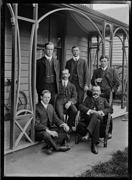 Six men, seated and standing, on a veranda, 1900