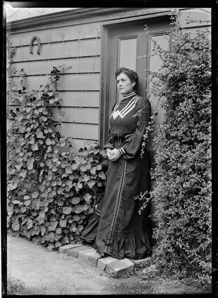 Woman standing on the doorstep of a weatherboard house, 1900