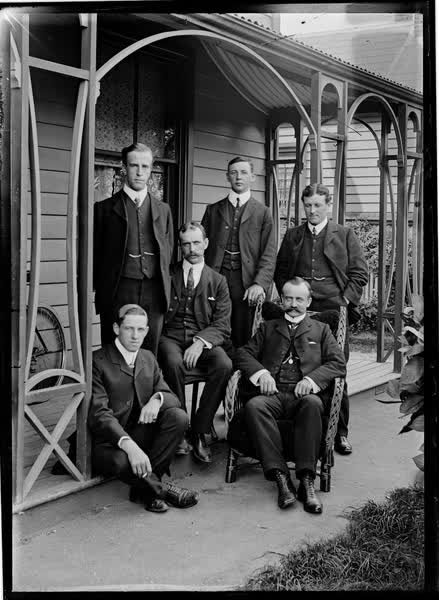 Six men, seated and standing, on a veranda, 1900