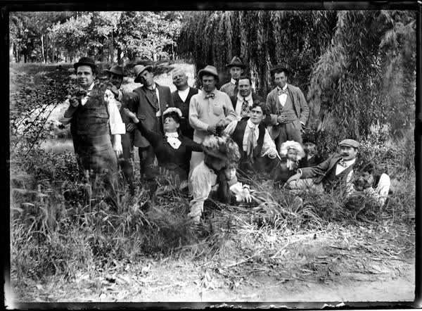 Sixteen men, women and children on the riverbank, 1900