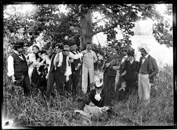 Fifteen men, women and children in front of a large tree, 1900