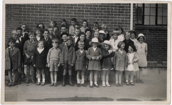 Children standing in front of a brick wall at Waimairi School, 1936