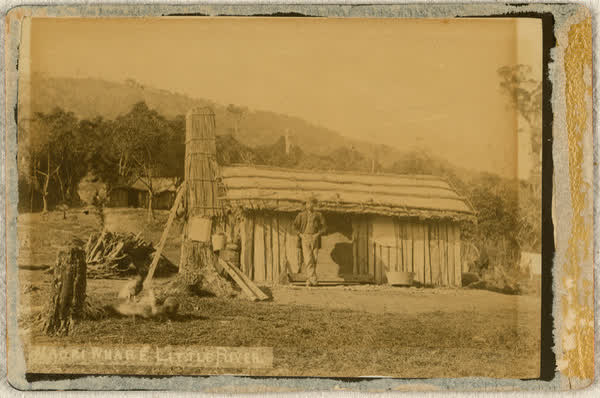 Unidentified man in front of a Māori whare in Little River, 1886