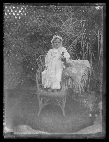 Child standing on a chair in a backyard, 1900