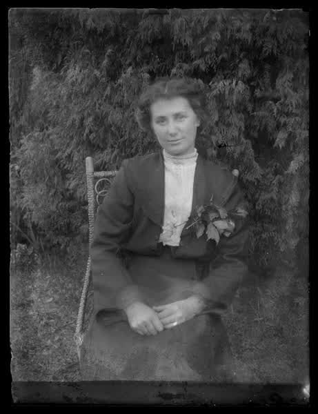 Woman sitting near bushes, 1900