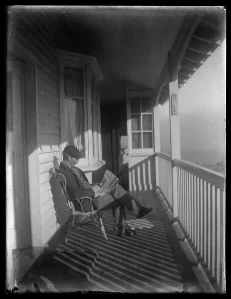 A man reading a newspaper on the verandah, 1900