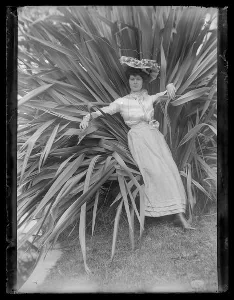 Woman leaning on harakeke or swamp flax, 1900