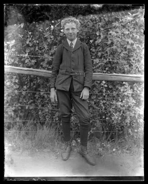 A boy standing by a fence, 1900