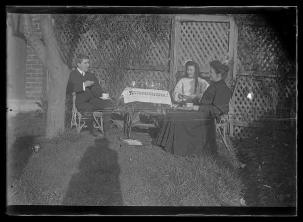 Three people having tea in the garden, 1900