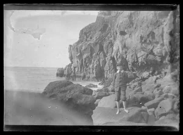Young boy at a boulder beach, 1900