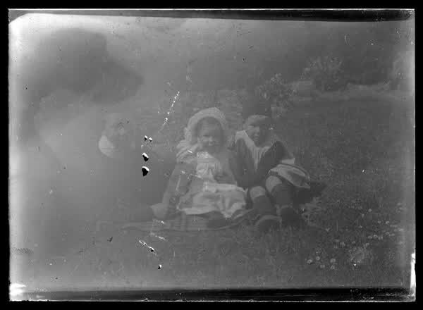 Three children sitting on the grass, 1900