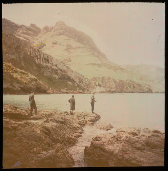 Three people standing on a coastline, 1950