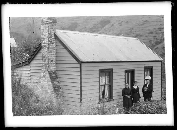 Two women and a man outside a house, 1900