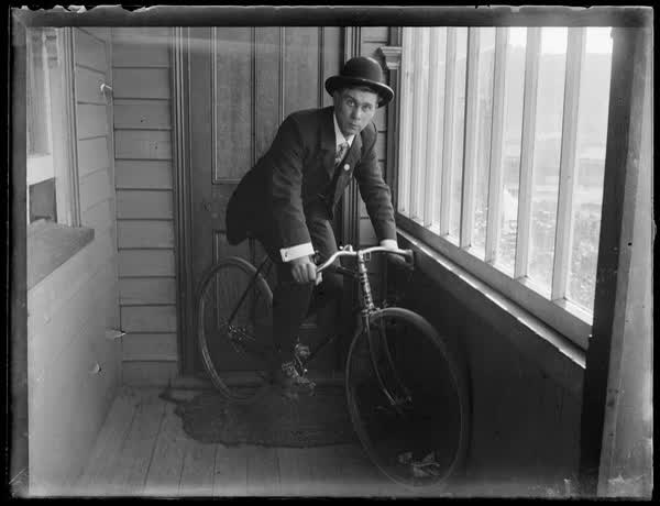 Man sitting on a bicycle indoors, 1900