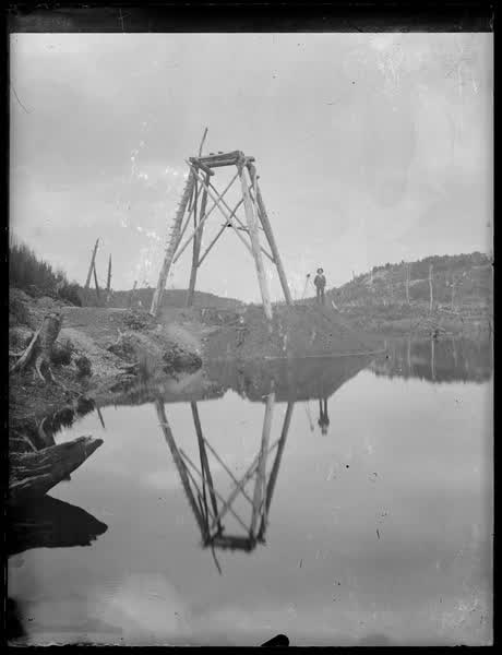 Two men beside a wooden structure, 1900