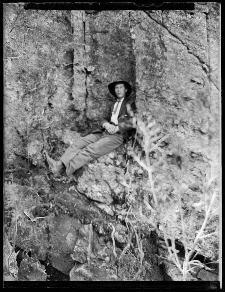 Man sitting on a rock ledge, 1900