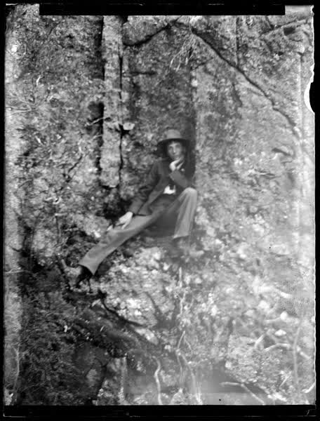 Man sitting on a rock ledge, 1900