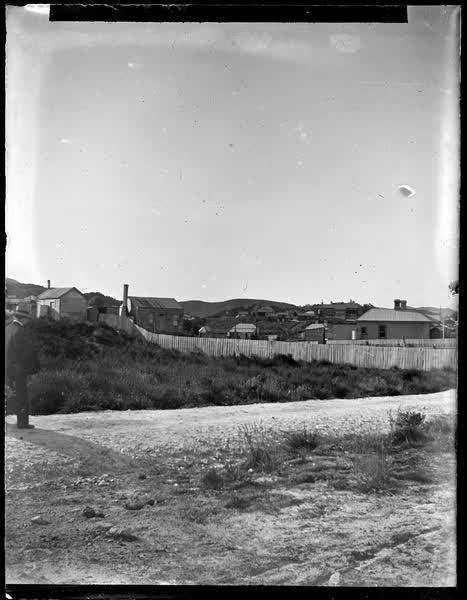 Man walking on round near houses, 1900