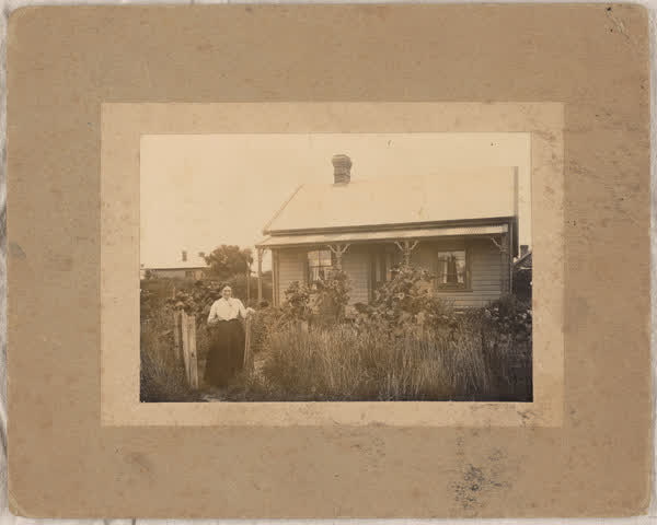 Woman outside a house, 1900